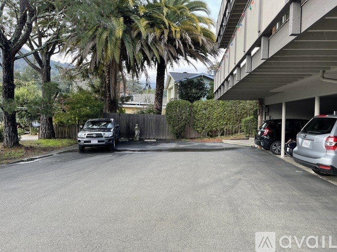 A car is parked on the side of a street with a fence and trees in the background.