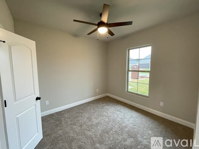 A room with a ceiling fan and a window overlooking a yard.