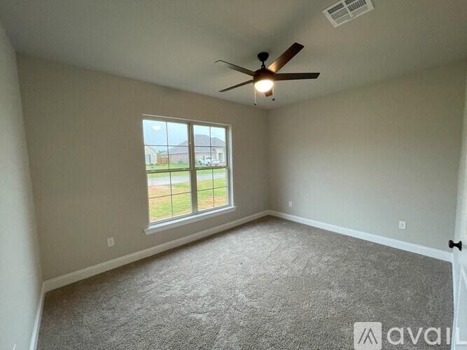 A room with a carpeted floor, a ceiling fan, and a window overlooking a yard.