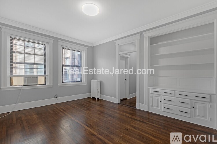 A room with wooden floors and white walls, with a window on the left and a door on the right.