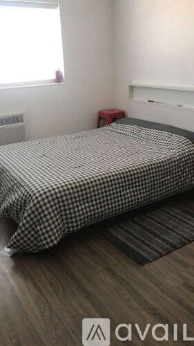 A bed with a checkered comforter and a red stool.