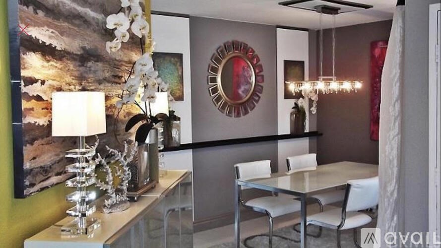A modern dining room with a large painting, a round mirror, and a chandelier.