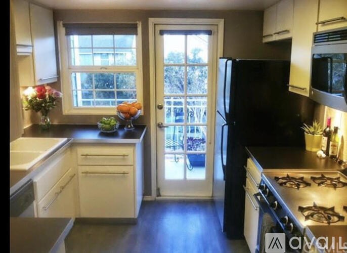 A kitchen with a black fridge and stove, white cabinets, and a window with a view of trees.