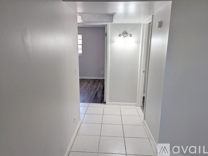A hallway with white tiled floors and white walls leading to a bathroom.