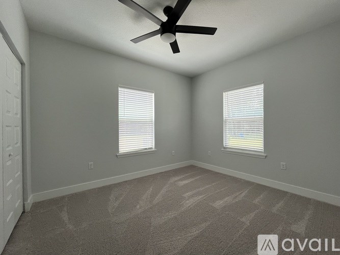 A room with a carpeted floor, a ceiling fan, and two windows with blinds.