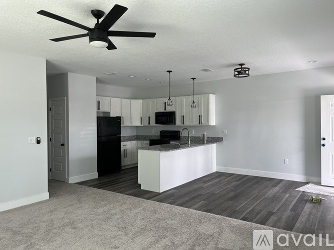 A spacious kitchen and living room with a ceiling fan and pendant lights.