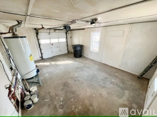 A spacious garage with a white wall and a black trash bin.