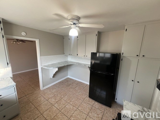 A room with a fan, a black fridge, and a white cabinet.