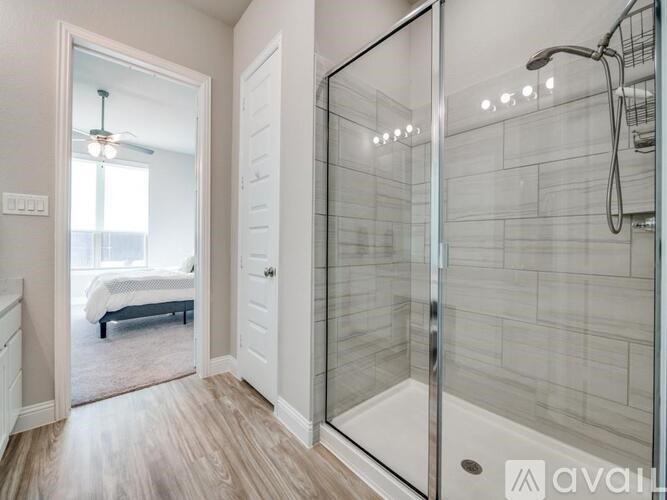 A bathroom with a walk-in shower and a bedroom with a bed and a window.