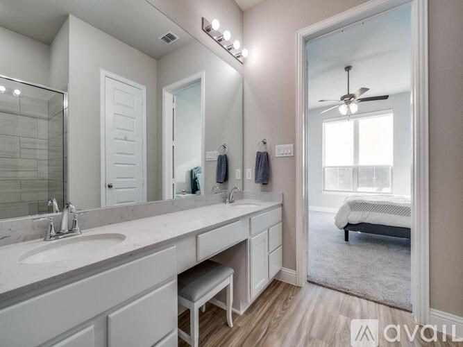 A bathroom with a vanity, mirror, and a bedroom in the background.