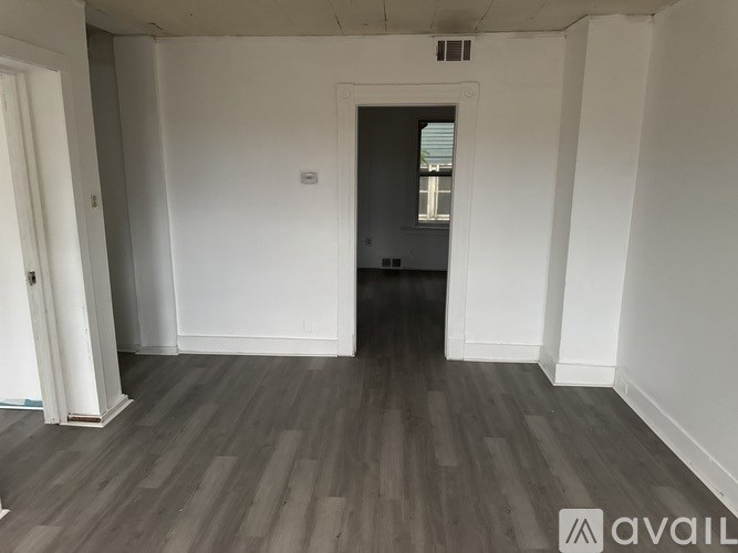 A room with wooden flooring and white walls, with a doorway leading to another room.