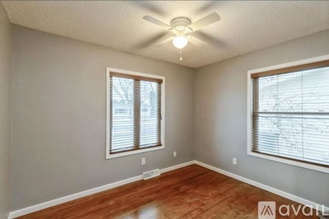 A room with a ceiling fan and two windows.