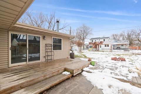 A house with a wooden deck and snow on the ground.