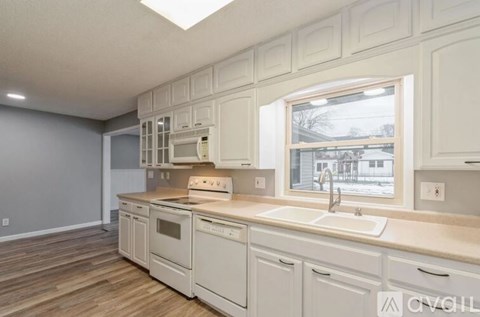 A kitchen with white cabinets and appliances, a window, and a wooden floor.