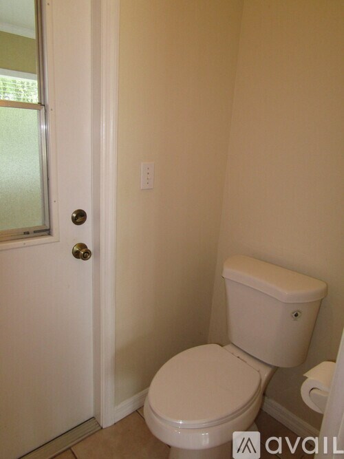 A white toilet in a small bathroom with a door and a window.
