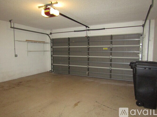 A large garage door is closed and there is a trash can to the right of it.