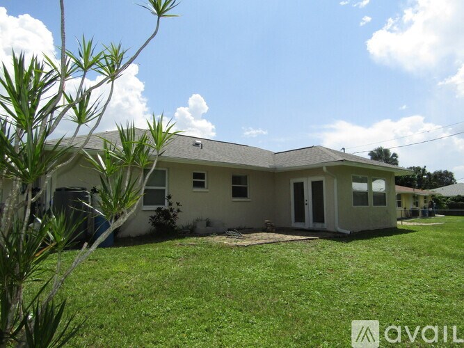 A house with a white exterior and a brown roof is surrounded by a grassy lawn.