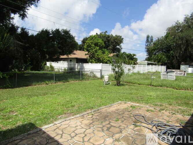 A backyard with a circular stone patio and a white fence.