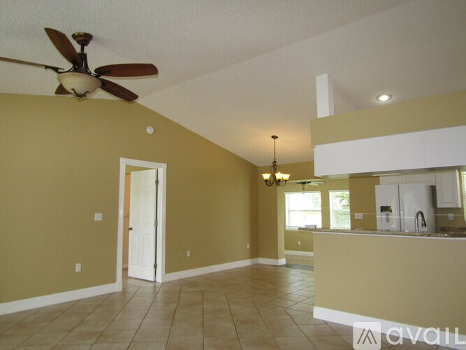 A room with a ceiling fan and a kitchen area in the background.