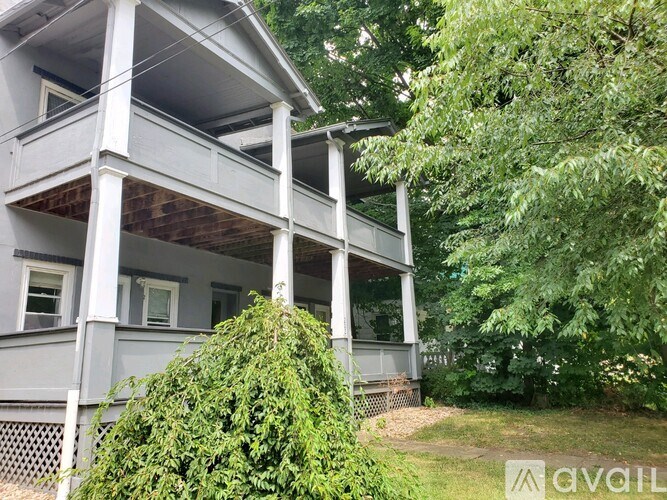 A white two-story house with a balcony and a tree in front.