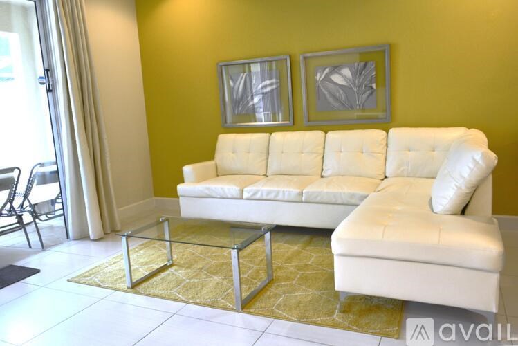 A white sofa with a glass coffee table in front of a yellow wall.