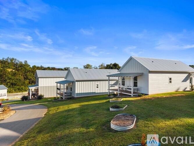 A large house with a metal roof and a covered porch is surrounded by a grassy lawn.