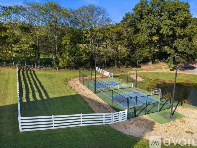 A tennis court is surrounded by a white fence and trees.