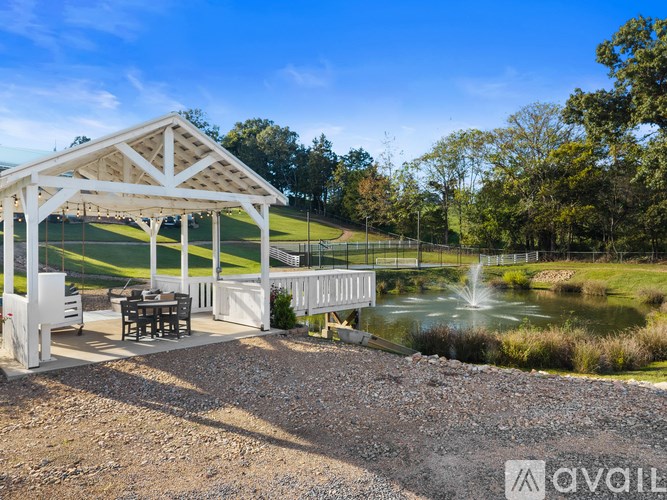 A pavilion with a table and chairs is situated by a pond.