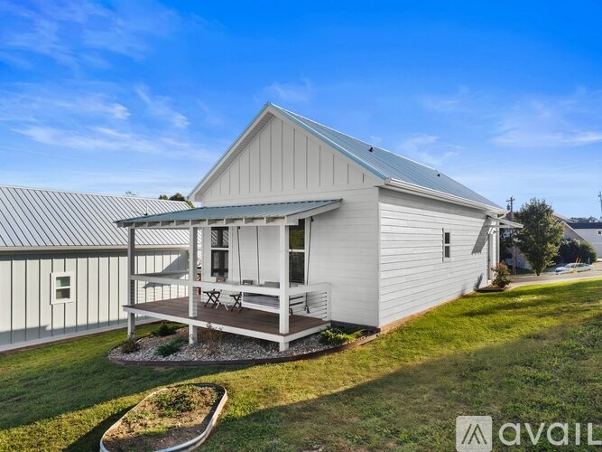 A white house with a metal roof and a deck in the front yard.