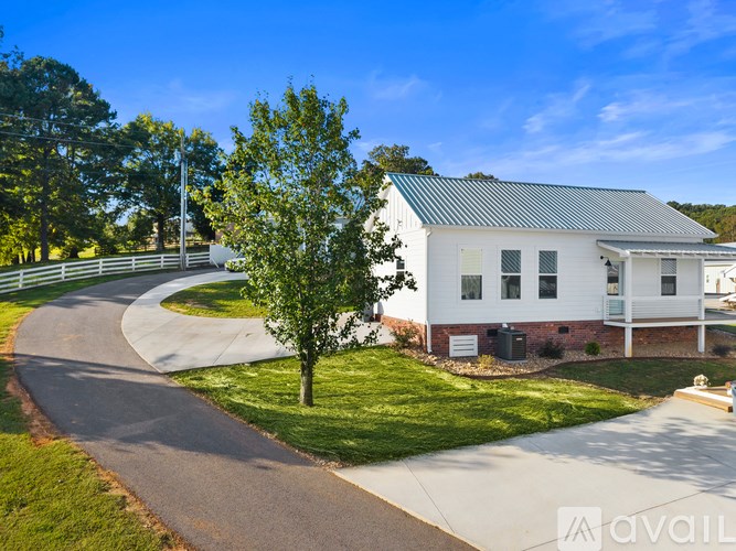 A white house with a green roof is surrounded by a grassy lawn and a curved driveway.