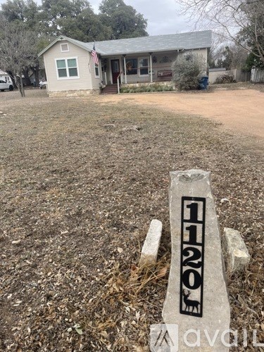 A white sign with the number 1120 on it is in the foreground of an image showing a house and yard.