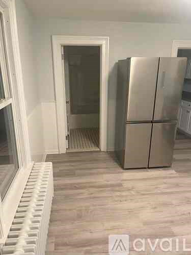 A room with a stainless steel refrigerator and a window with a radiator below it.