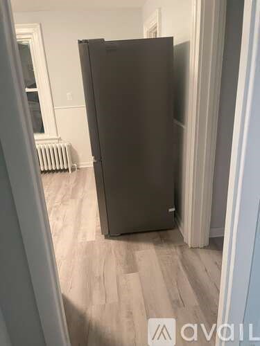 A black refrigerator in a room with wooden flooring and white walls.