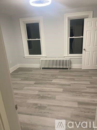 A room with a white door, two windows, and a radiator on the floor.