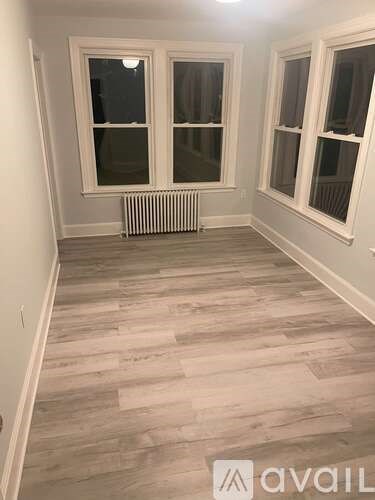 A room with wooden flooring and a radiator between two windows.