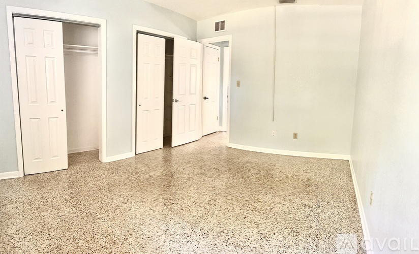 A room with a speckled floor and white walls has four doors.