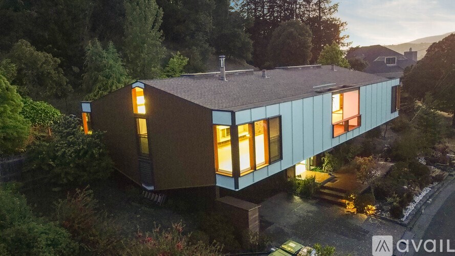 A modern house with a flat roof and large windows is surrounded by greenery.