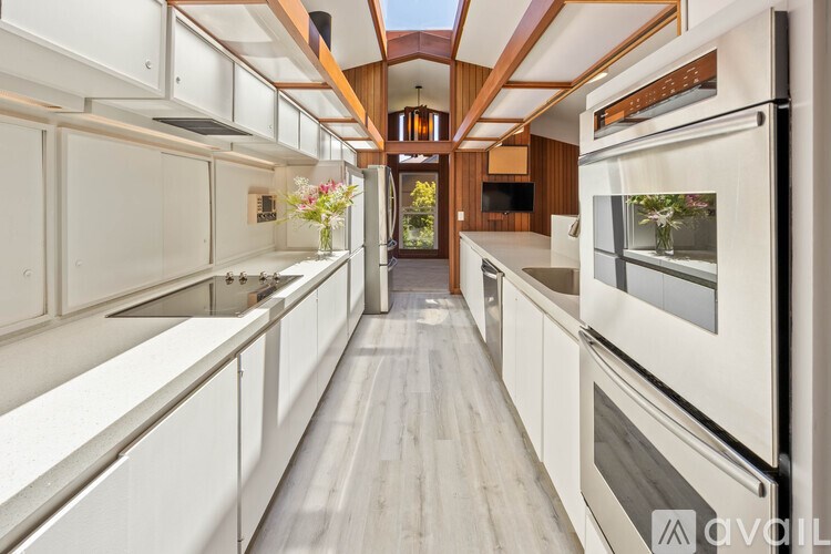 A modern kitchen with white cabinets and a long wooden floor.