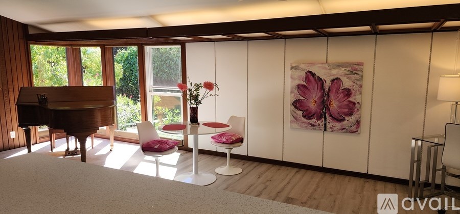 A room with a piano, a chair, a vase with flowers, and a painting on the wall.