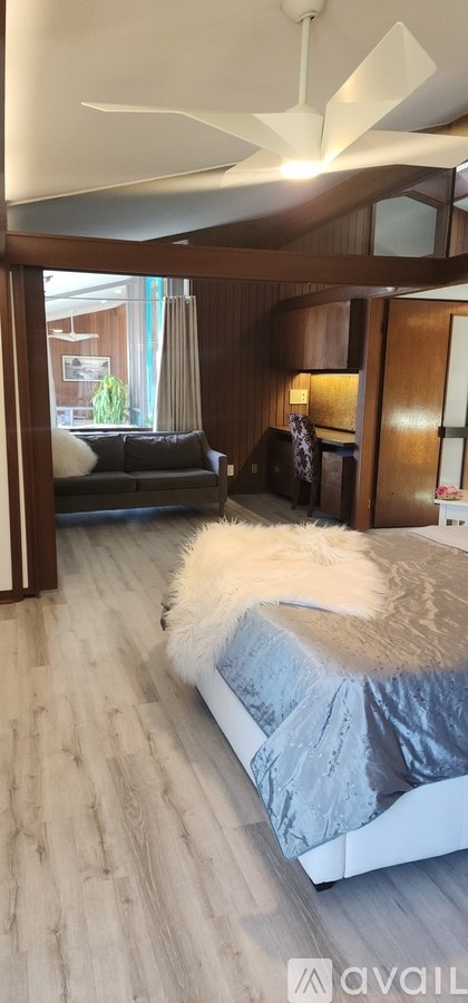 A white fluffy cat is sitting on a grey bed.