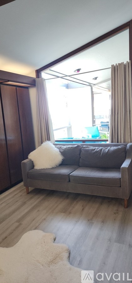A grey couch with a white pillow is in front of a sliding glass door.