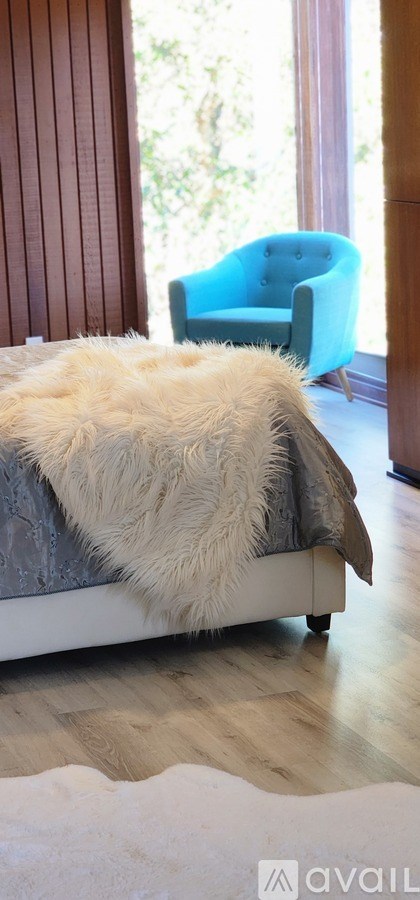 A blue chair sits in front of a window in a room with a white couch and a white fur throw.