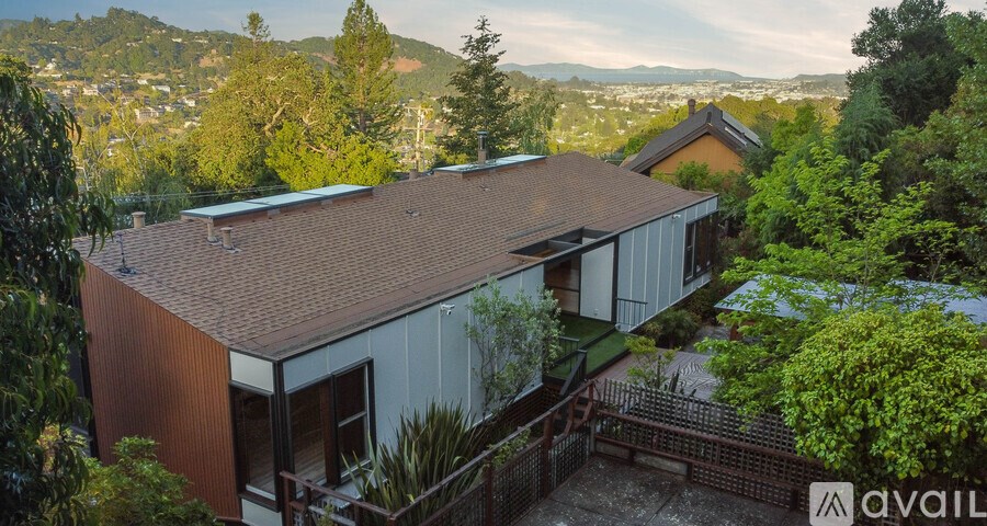 A house with a brown roof is surrounded by greenery and has a mountain in the background.