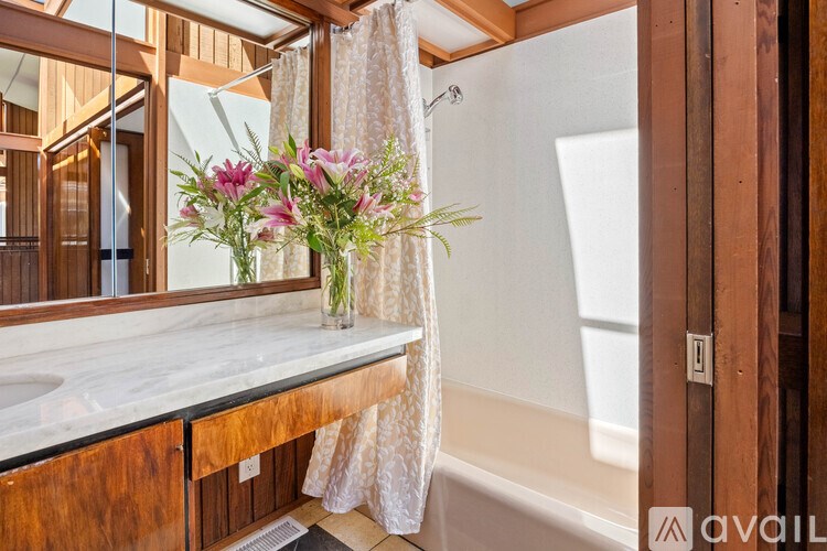 A wooden bathroom with a marble counter and a vase of flowers.