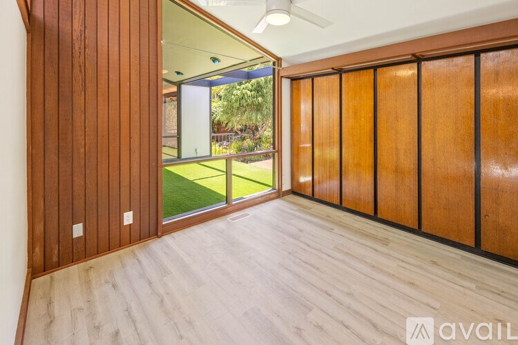 A room with wooden walls and floor and a sliding glass door leading to a green lawn.