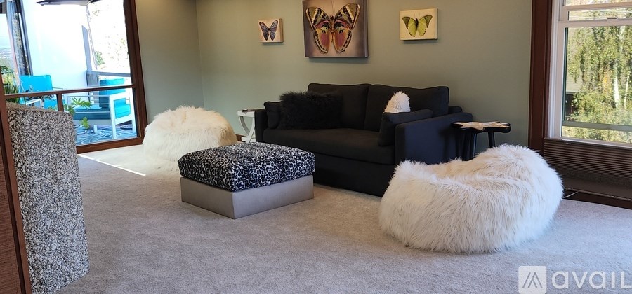 A living room with a black couch, a white fluffy chair, and a grey ottoman.