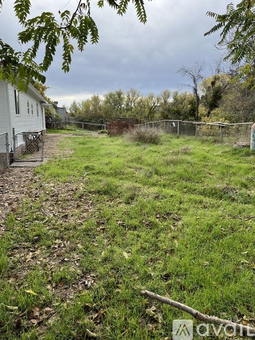 A grassy area with a white house and a fence in the background.