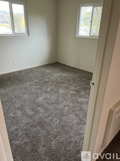 A room with a grey carpet and two windows.