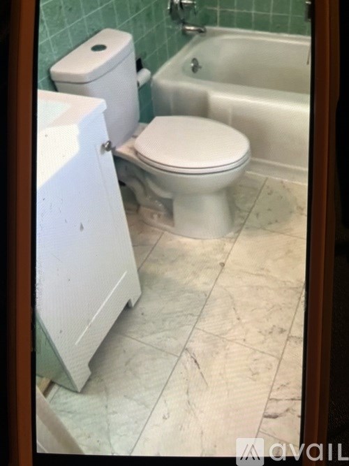 A white toilet is in a bathroom with a white bathtub.
