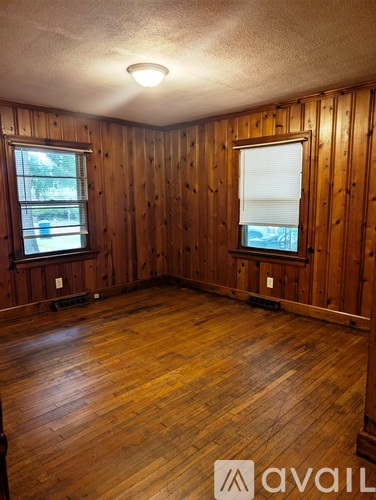 A room with wooden walls and floors and two windows.